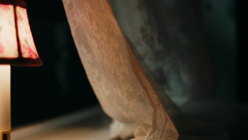 Lace curtain sways gently beside a lit lampshade