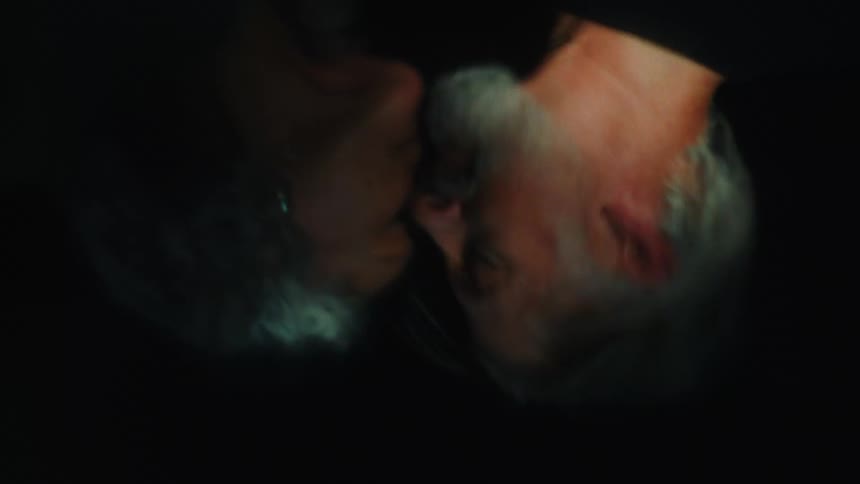 A closeup of a couple kissing reflected on a dark water surface