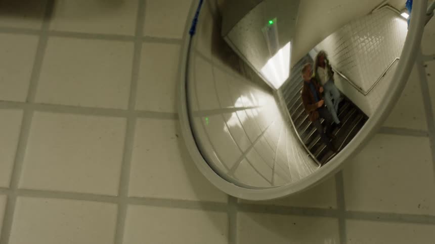 Couple is seen walking down the stairs through the reflection of a convex mirror