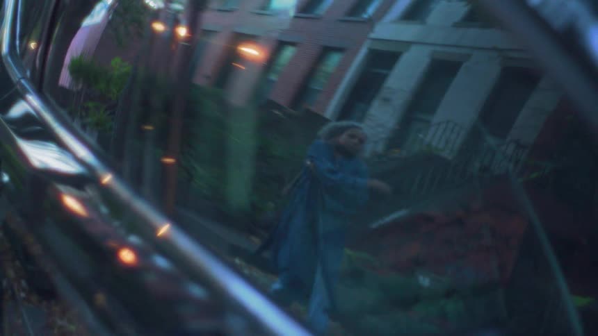 The reflection of a woman walking along a street is seen in a car window