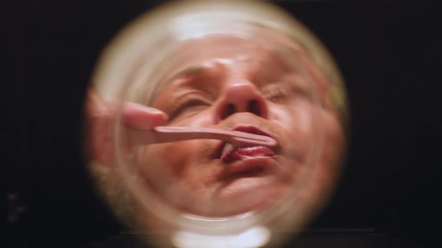 The face of a woman brushing her teeth and then spitting into a sink