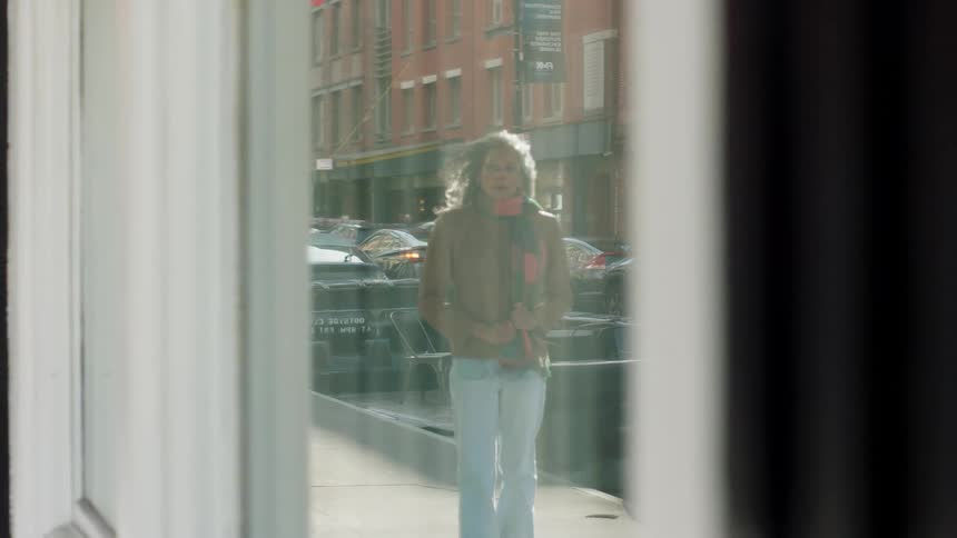 Woman walks along the sidewalk on a sunny day as seen through a storefront window