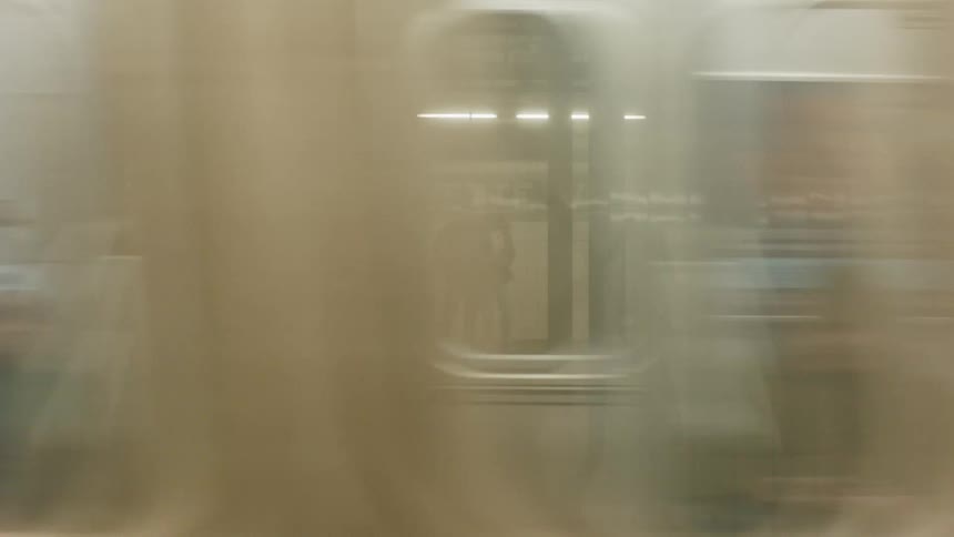 The camera is inside a subway car as it moves rapidly showing the blurry platform environment including an american flag motif and signs the train then stops revealing a couple standing closely together on the lafayette subway platform framed by th