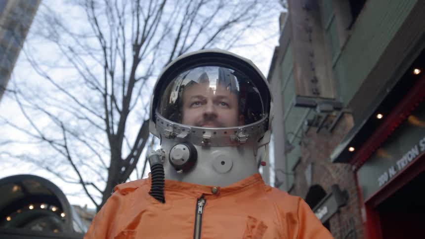 Man wearing astronaut suit walking on city sidewalk