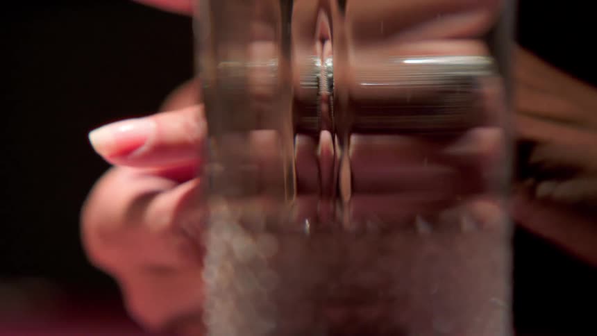 A close up shot focused on a clear glass with water on it and a female human hand behind it on an indoor setting with a dark background
