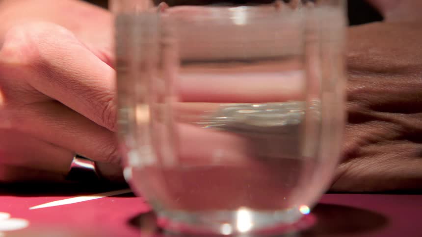 Seen through a glass of water a man slips a sparkling diamond ring onto a womans finger