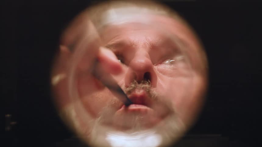 Man appears distorted through a circular lens while brushing his teeth