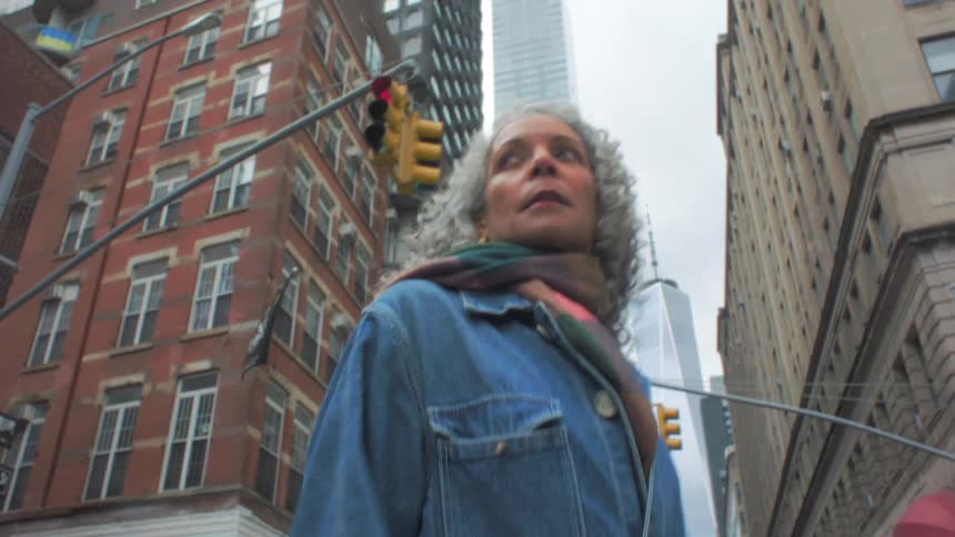 Woman looks around as she crosses a downtown street with apartment buildings and skyscrapers in the distance