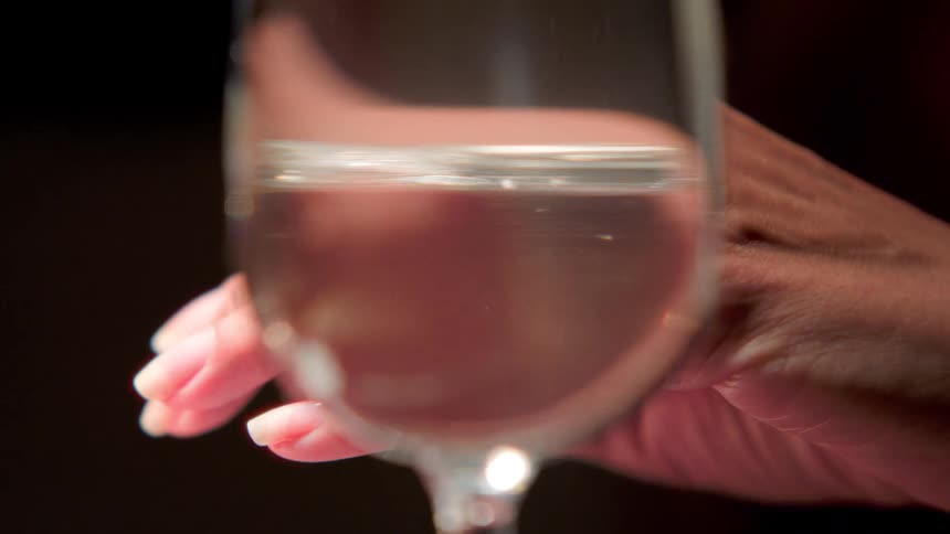 A hand appears blurred behind a clear glass of water that sharply distorts its shape