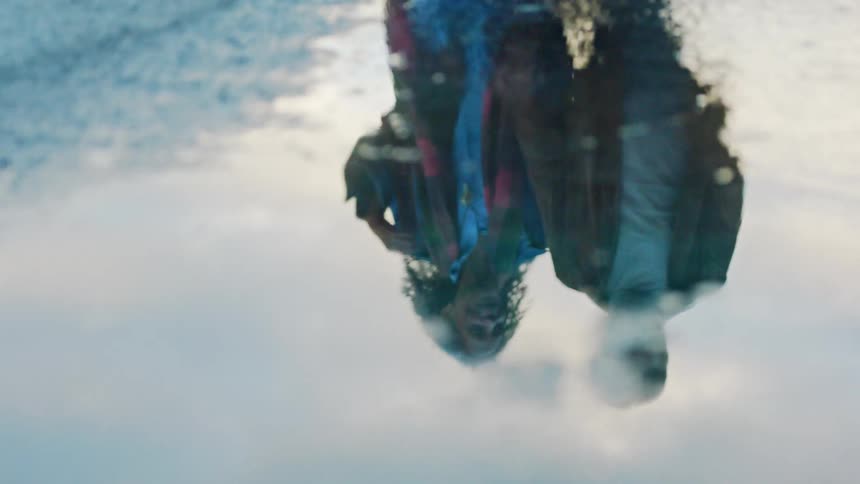 Reflection of two people in puddle on wet ground with cloudy sky in the background
