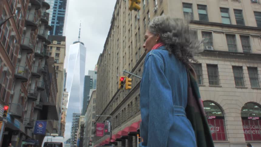 Woman looks around as she crosses a downtown street with apartment buildings and skyscrapers in the distance