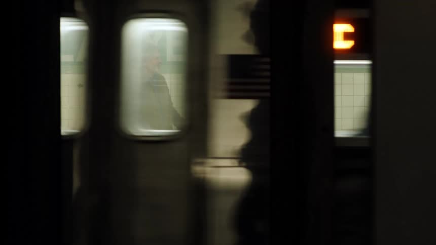 An older couple embraces on a subway platform next to a tiled wall reading lafayettea train pulls quickly into the station briefly obscuring the couple before they reappear inside the train windows still holding one another