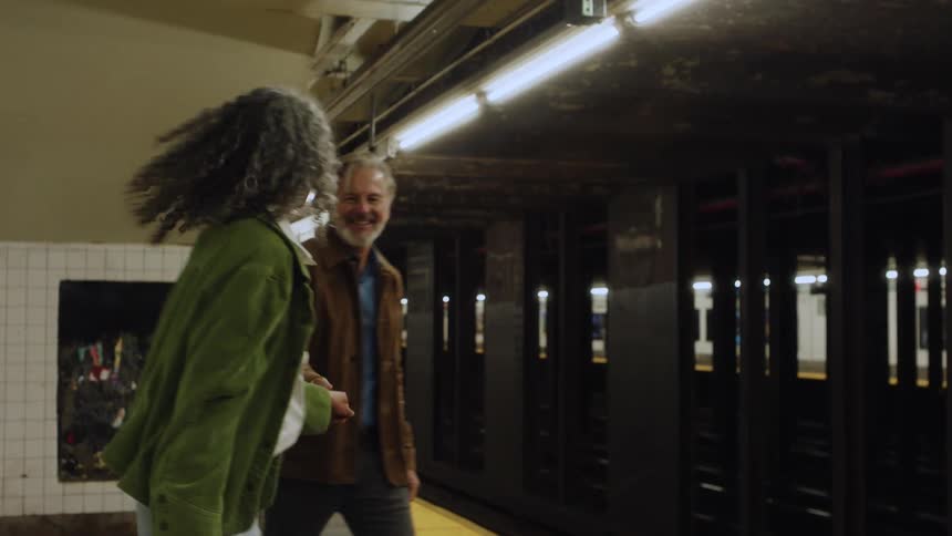 A man and woman dance and hug while waiting on a subway landing