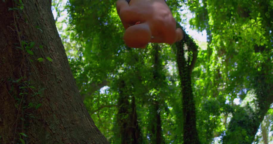 A shirtless man performs a backflip in a sunlit forest