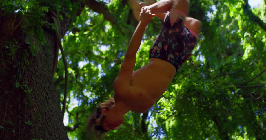 A young man flips backward in mid air among dense green forest leaves
