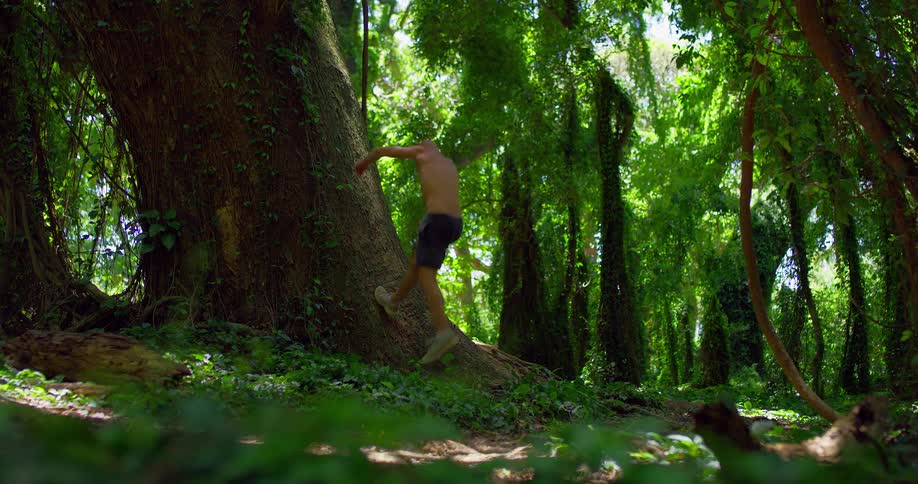 Man wearing shorts runs to a bent tree trunk and does a somersault flip in mid air