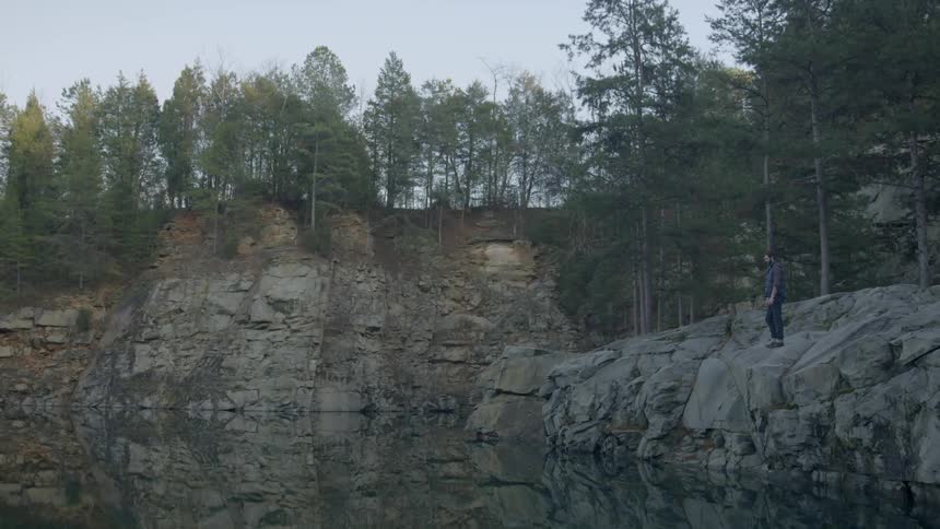 Man stands at the edge of a rocky cliff overlooking a lake