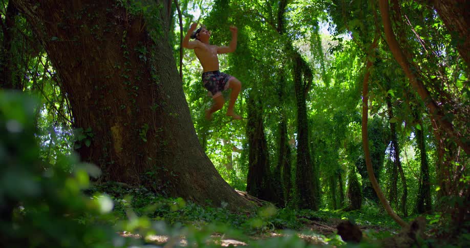 An athletic man jumps and somersaults off of a large tree trunk