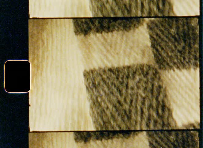 A vintage film strip scrolls vertically displaying the fuzzy woven texture of a checkered fabric