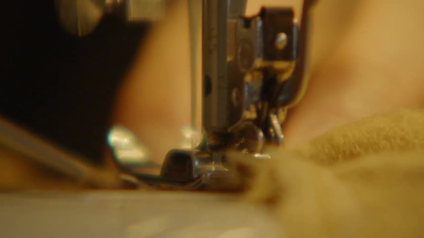 Person uses a tool to push fabric under the foot of a sewing machine