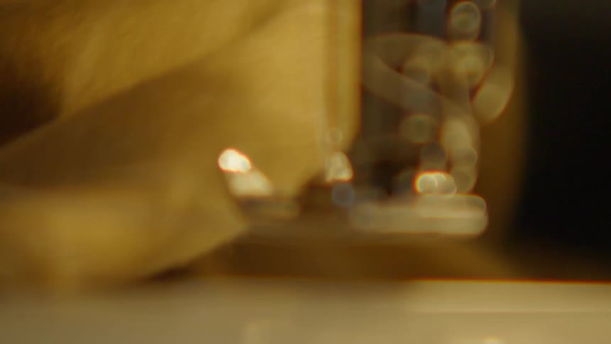Needle and presser foot stitch fabric on sewing machine under warm lighting