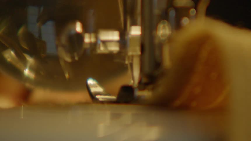 Needle and presser foot stitch light fabric on sewing machine with metallic components in focus