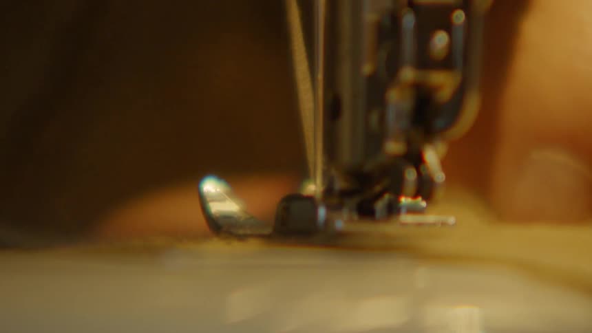 The sewing machines needle and presser foot move rapidly up and down stitching fabricthe camera focuses tightly on the mechanical parts and the thread highlighting the detailed process of garment construction
