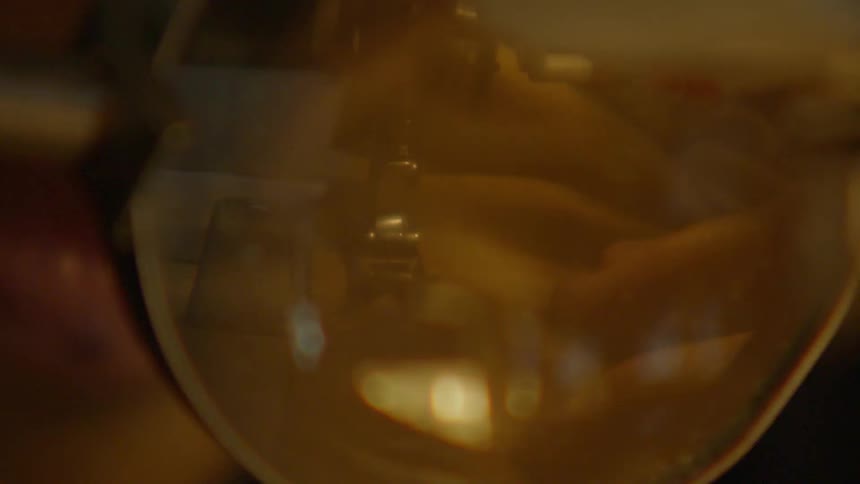 A viscous goldenamber liquid is slowly poured into the glass causing the liquid already inside to swirl and reflect the lightthe focus is on the glasss rounded bottom and the thick texture of the substance suggesting a scientific experiment brewi