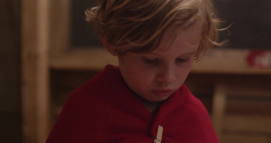 A boy is wearing a blanket cape held on by a clothes pin