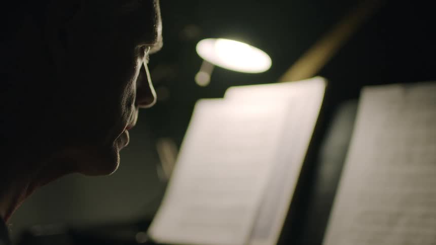 Man sits in a dark office looking at sheet music