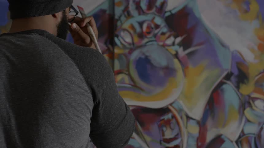 A man paints on a wall then pushes up his glasses