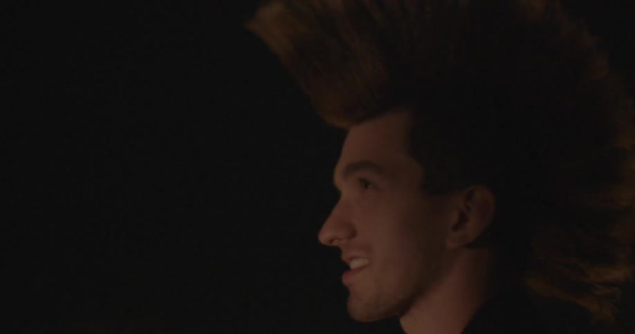 A man with spiked hair is watching and talking to someone