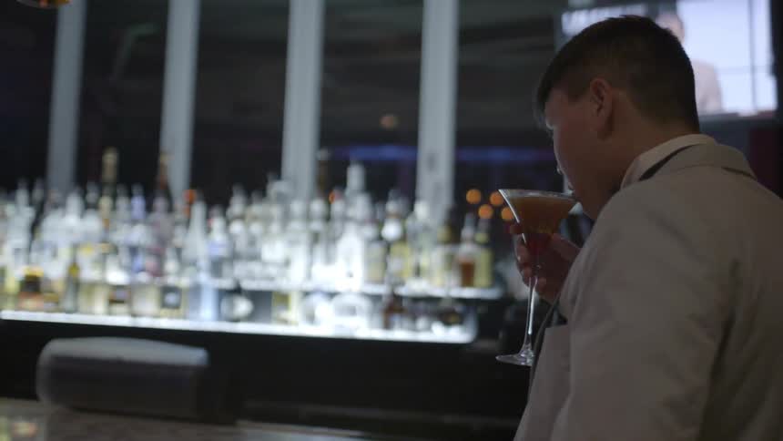 A man sips from a martini glass and puts it back on the bar