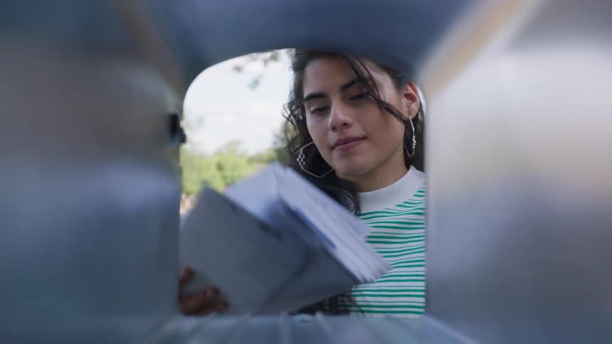 Young woman opens her mailbox and takes out her mail