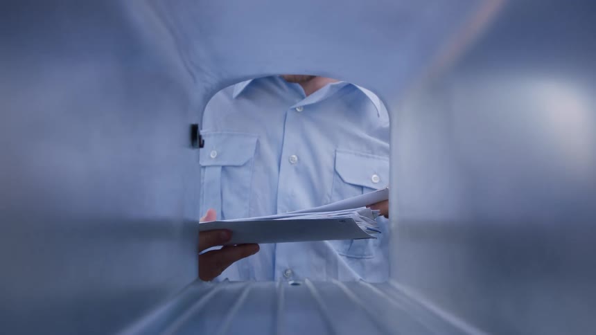 Male postal worker places mail into a mailbox during the daytime