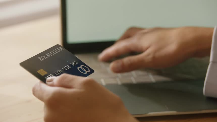 Person holding a credit card and typing on the keyboard of a laptop computer then putting the credit card into its case