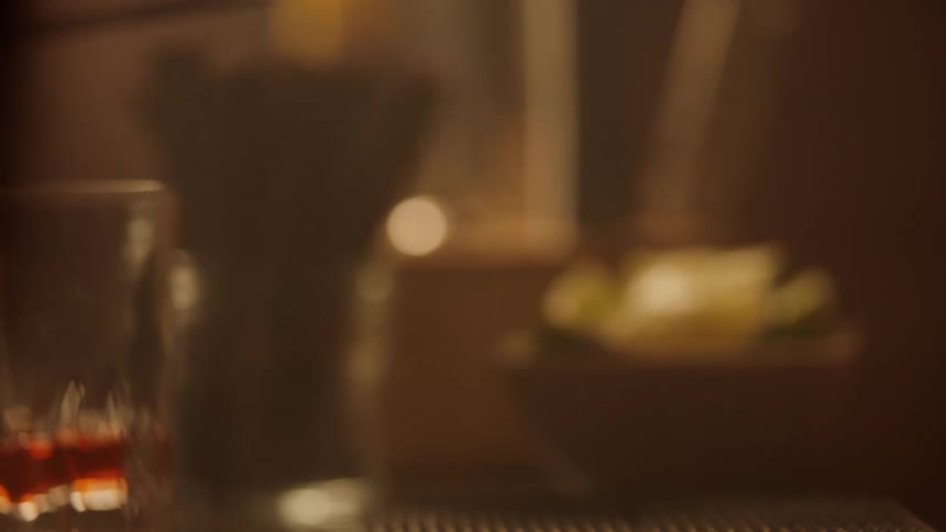 The video is dark focusing on two hands holding a slender ornate bar spoon the spoon appears to be used for stirring set against a blurred background with a dimly lit drink glass