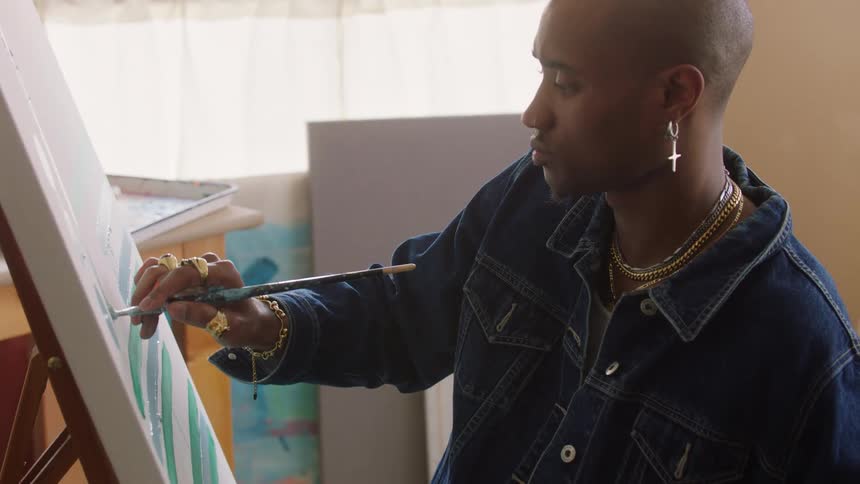 A man is carefully using a paintbrush to draw a downward line on a whiteboard