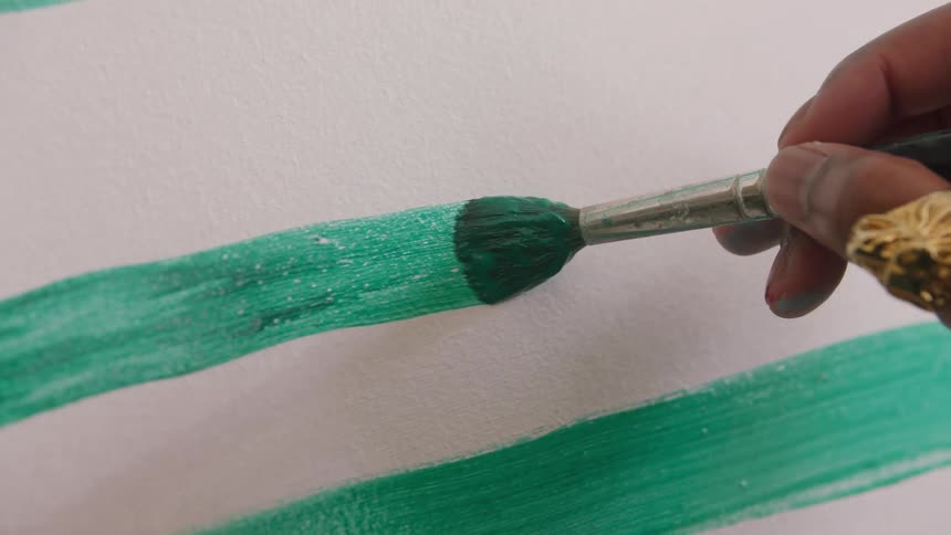 Hand with gold ring applies green paint on white surface