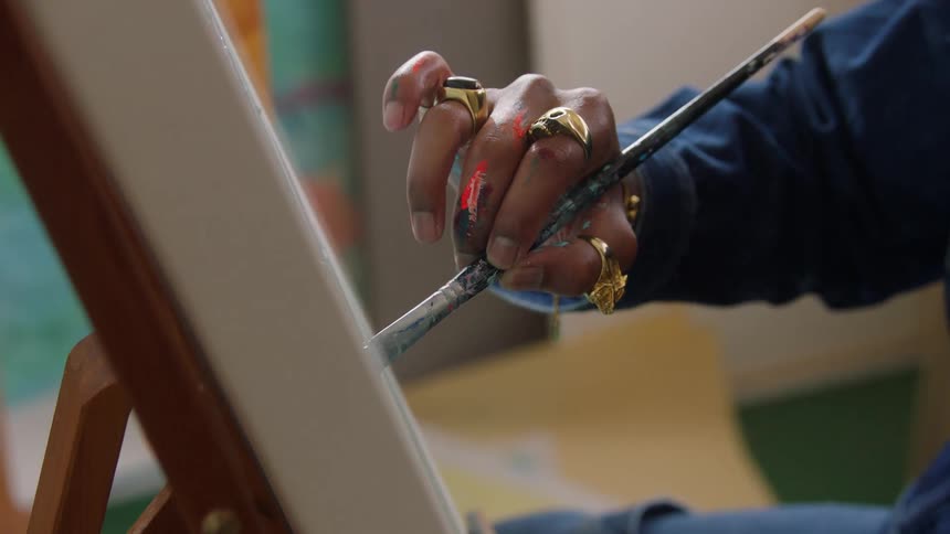 An artists paint stained hand adorned with gold rings carefully applies a brushstroke to a canvas