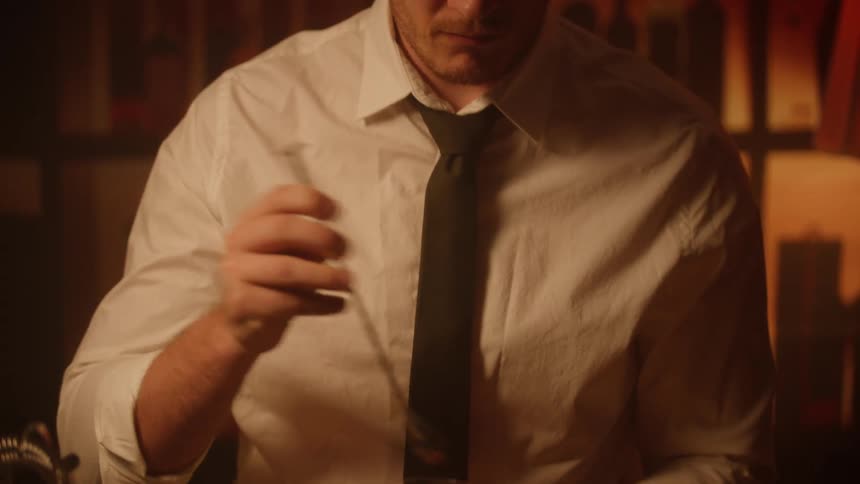 A person using a metal object to stir a glass of drink with ice inside