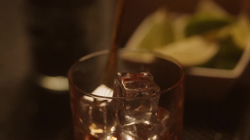 Person tending bar pours liquor into a glass filled with ice