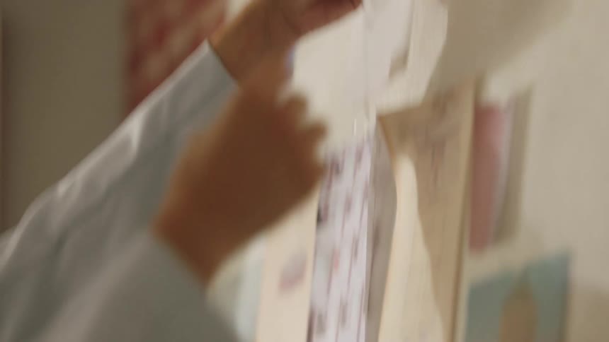 A hand wearing the cuff of a light blue blazer with brass buttons holds a small hangs paper on a textured wall