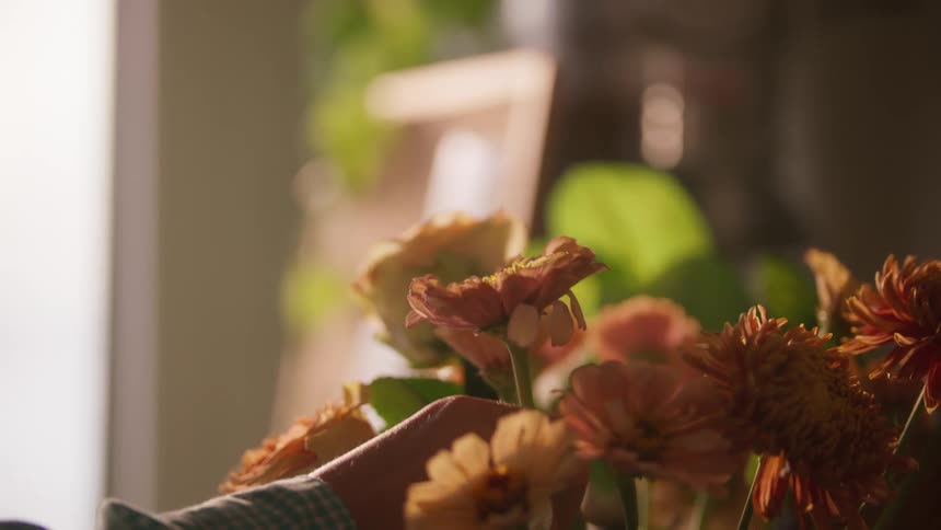 A woman picks up a single flower from a flower arrangement