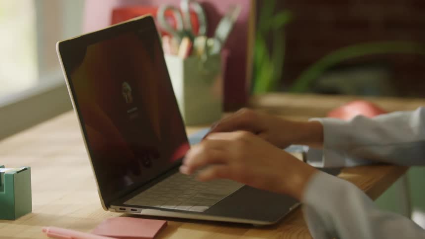 Person typing on laptop with login screen on wooden desk surrounded by stationery items