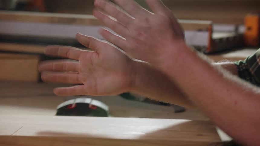 A man claps his hands together over a workbench sending fine particles of sawdust into the air after working on a piece of wood