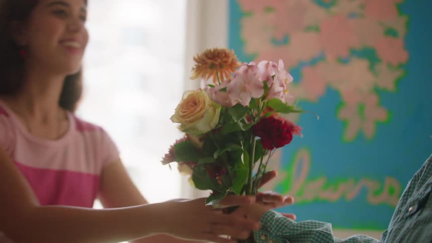 Person hands bouquet with lilies roses and chrysanthemums in front of colorful panel with pink tree