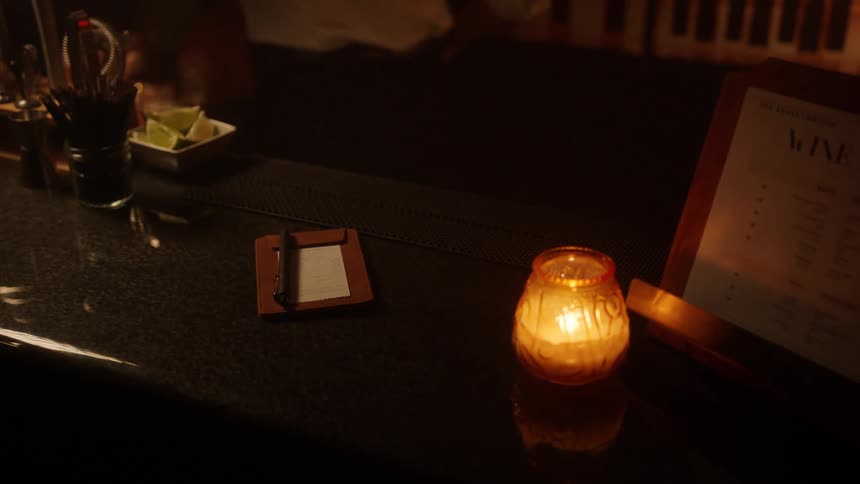 Male bartender places an ordering pad on the bar counter before wiping a glass