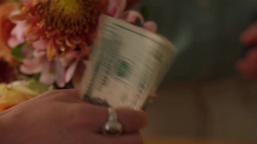 Person holds cash beside a bouquet suggesting the purchase of flowers