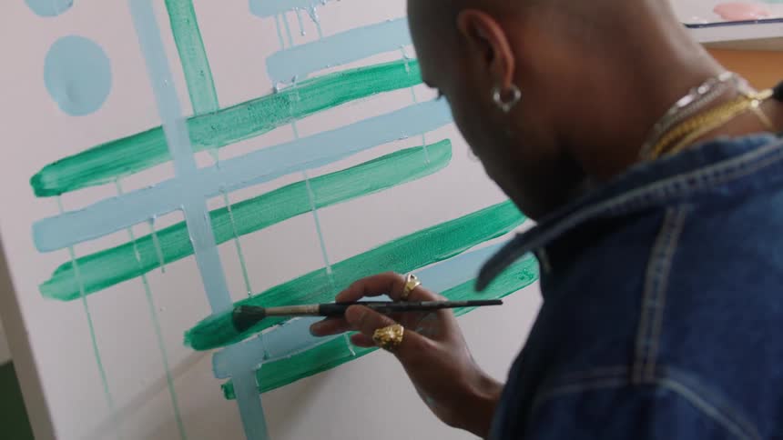 Artist applies green and blue brushstrokes on a canvas with geometric patterns